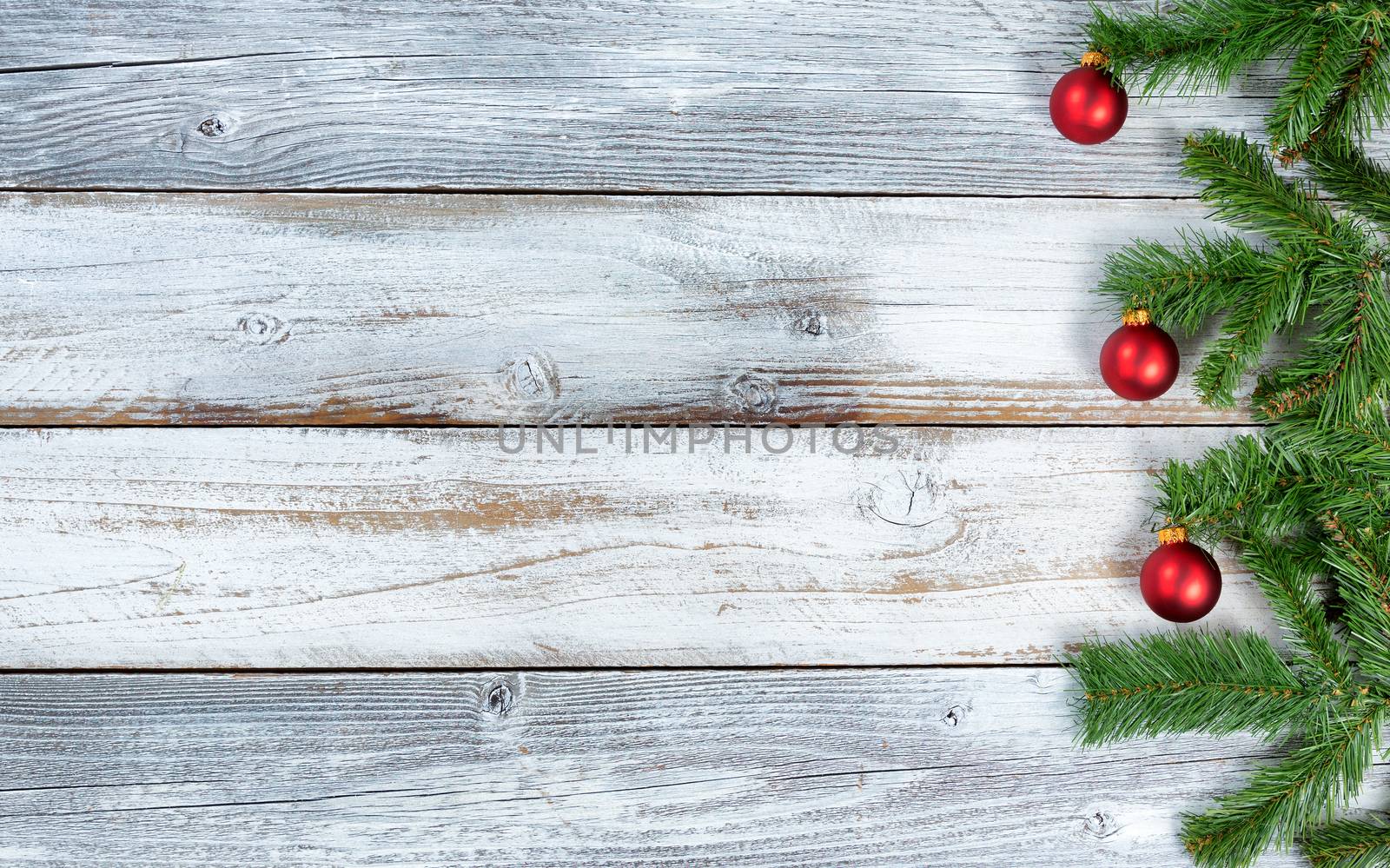 Christmas evergreen branches and red ornaments on rustic knotty  by tab1962