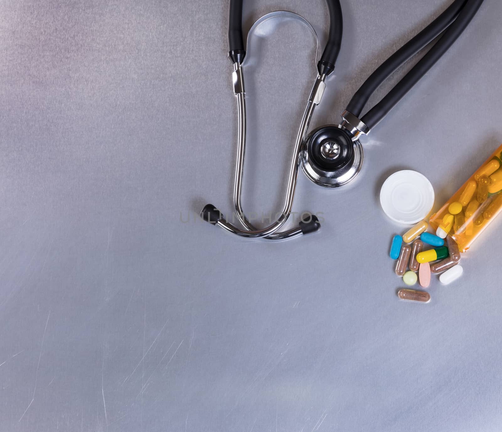 Overhead view of a medical stethoscope and pills on stainless steel table