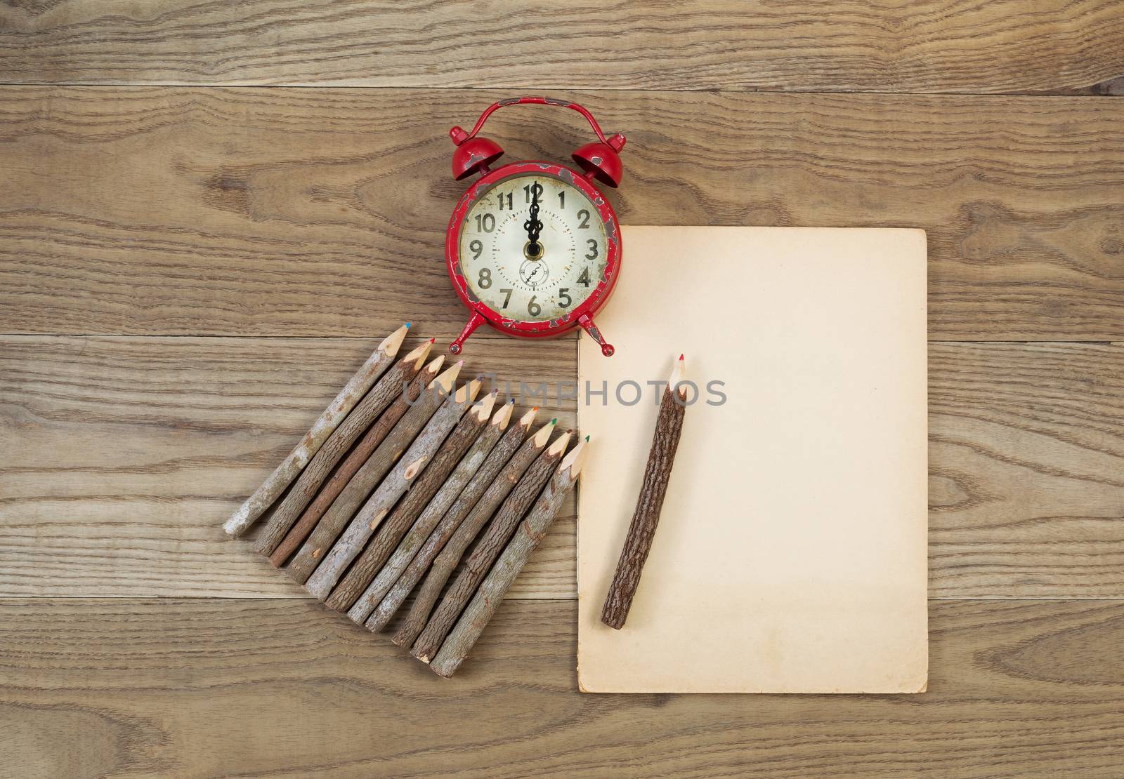 Overhead view of old pencils with tree bark, aged paper and alarm clock on rustic wood