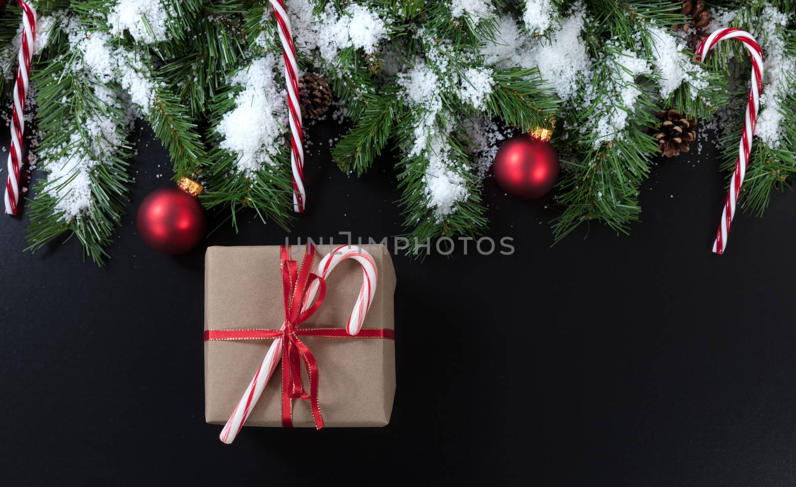 Christmas gift with snowy evergreen tree branches, candy canes and red ornaments on black background 