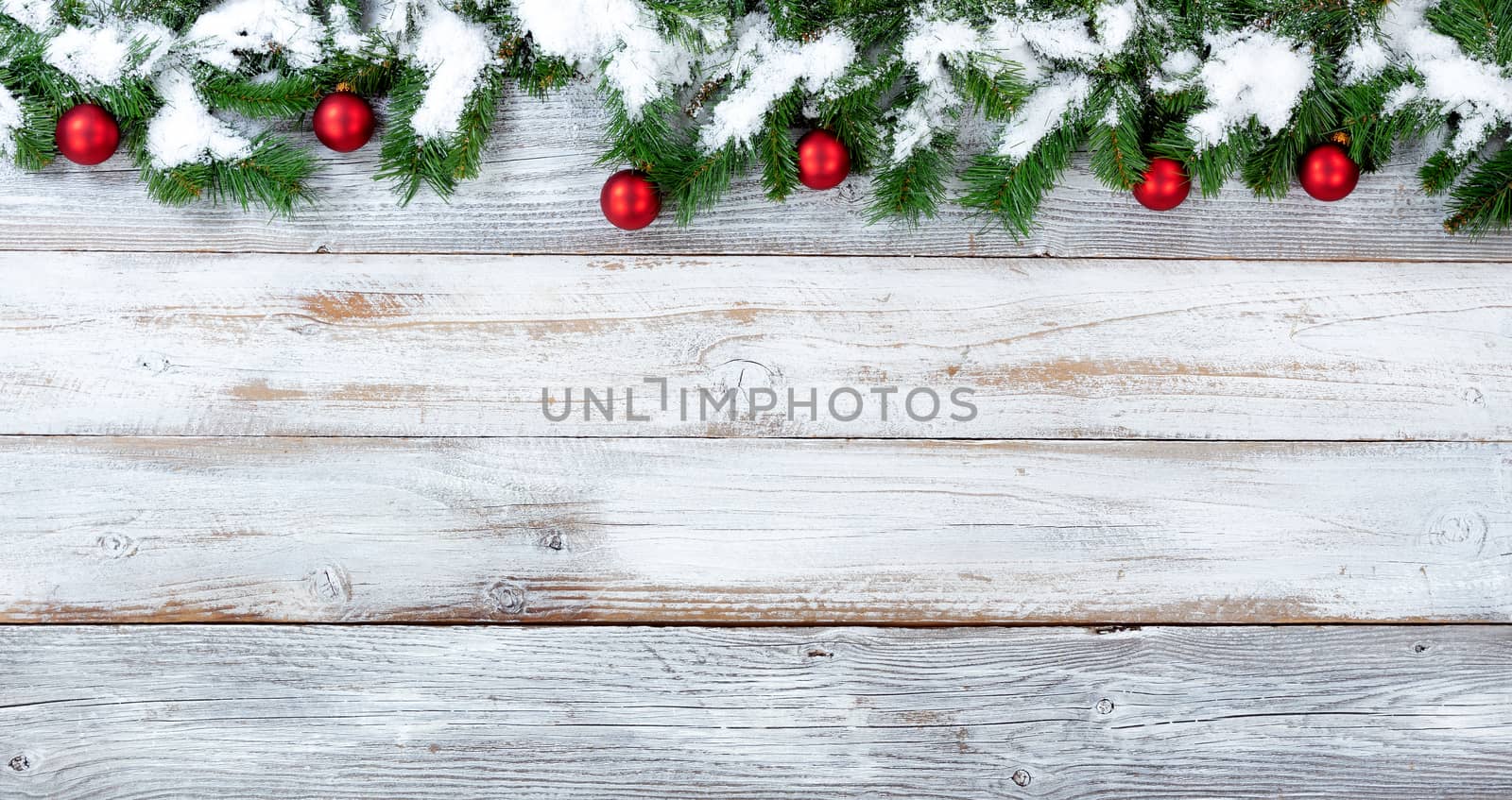 Snow covered top border of Christmas evergreen branches and red ornaments on white vintage wood
