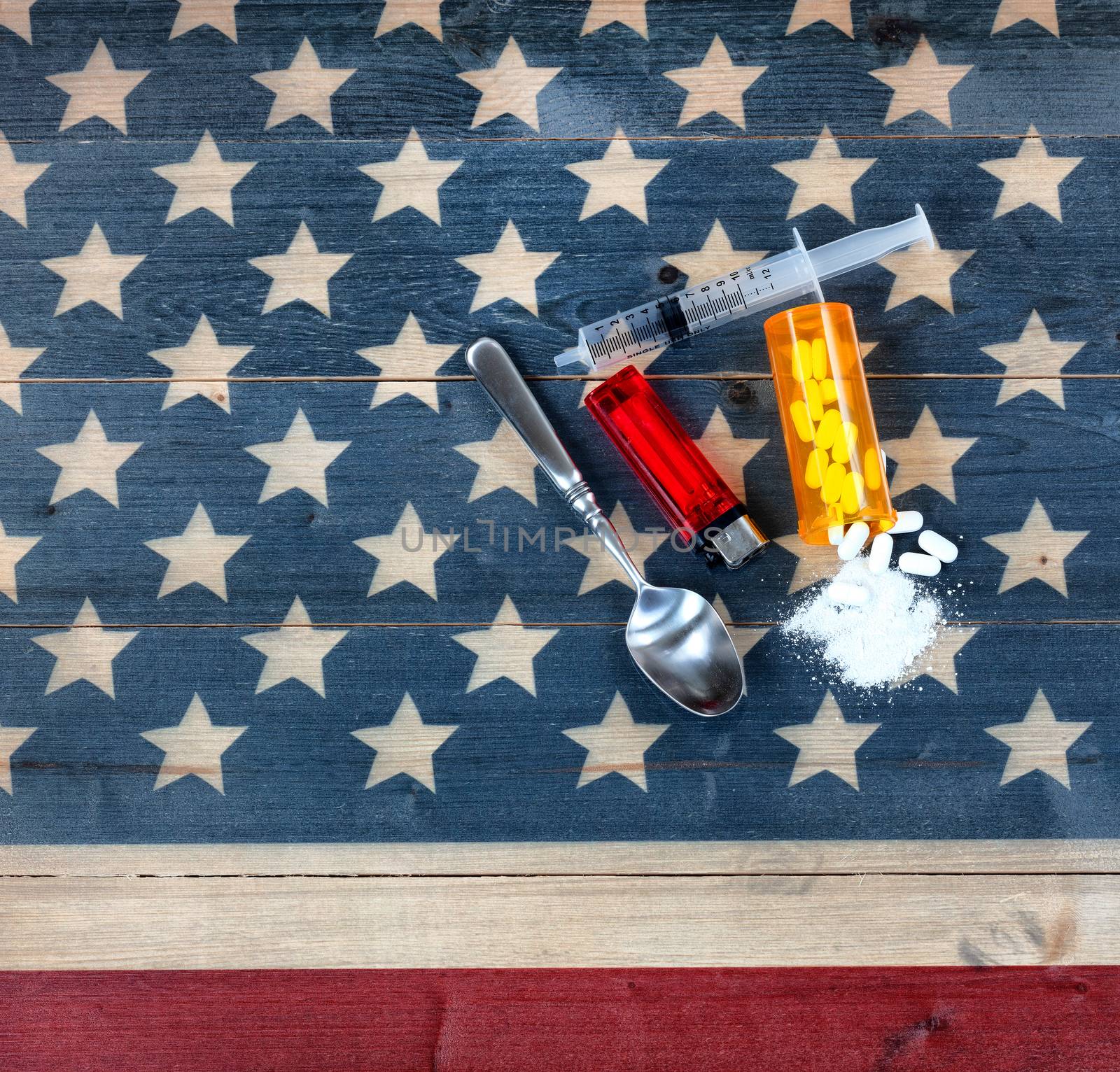 Overhead view of opioid pain killer tablets with spoon, lighter and syringe on rustic USA flag in background for drug addiction concept in America  