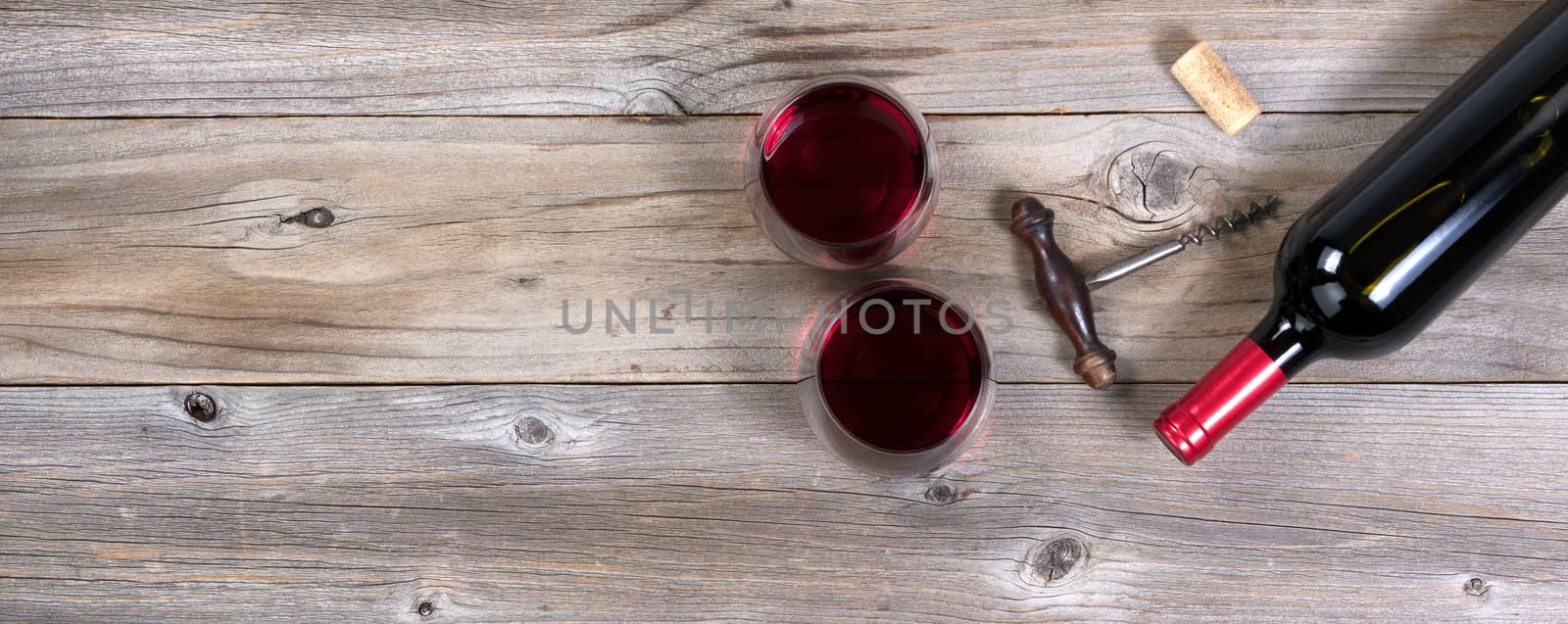 Flat view of a bottle of red wine, antique corkscrew, and full drinking glasses on rustic wooden boards