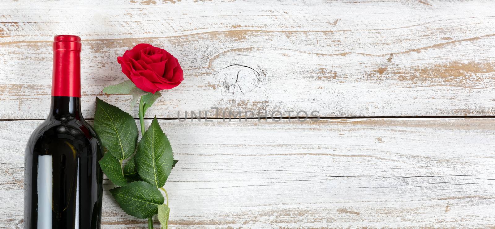 Romantic Valentines Day celebration with red wine and a single rose on white rustic wood 