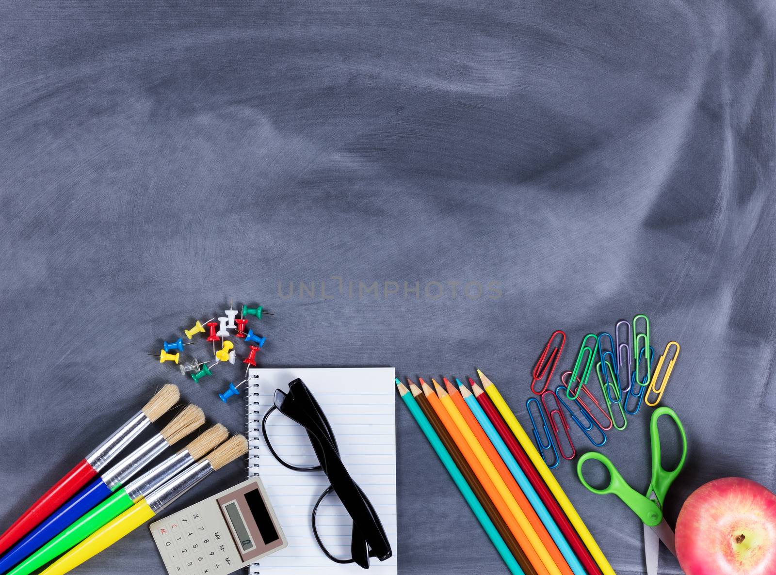 Overhead view of back to school supplies positioned on bottom part of erased chalkboard. 