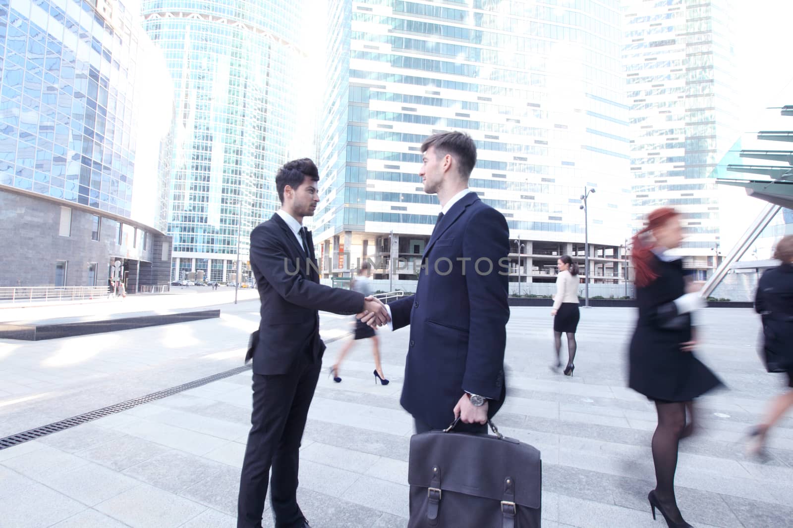 Business people shaking hands in street , crowd around, skyscrapers on background