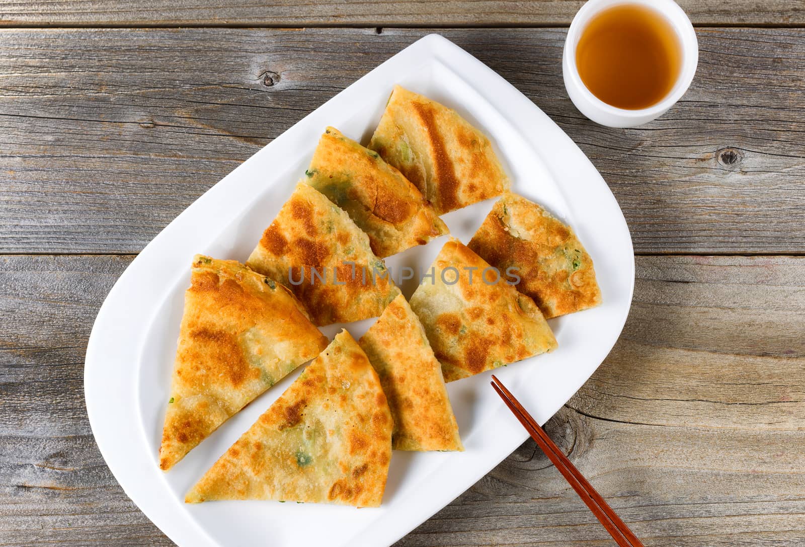 Top view of fried Asian pancakes with green tea and chopsticks on white plate. Rustic wooden boards underneath. 