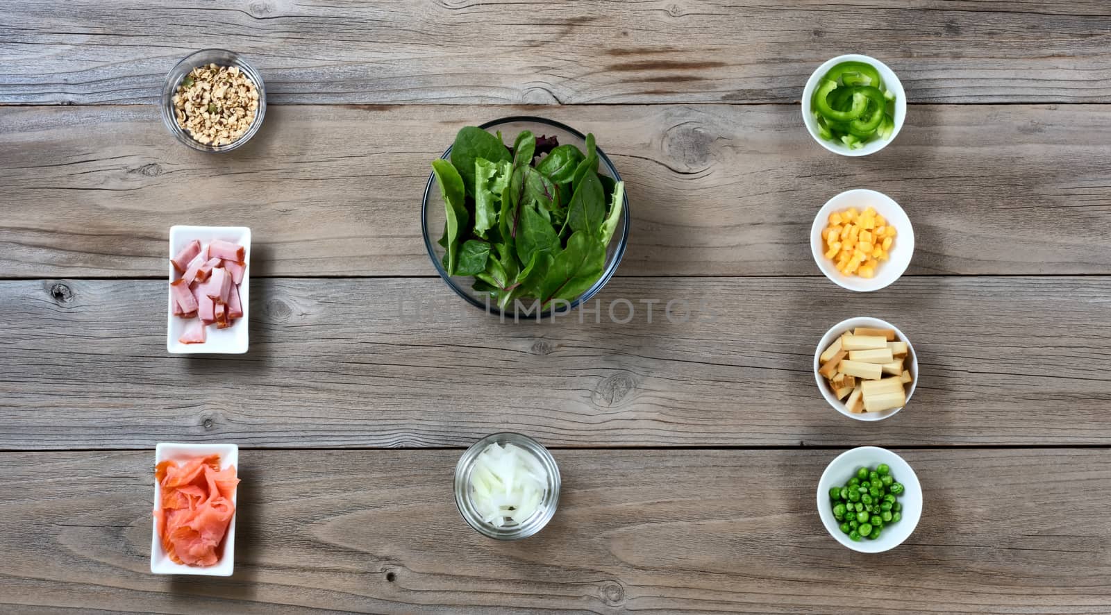 Bowl of green leaf salad with side ingredients on rustic wood  