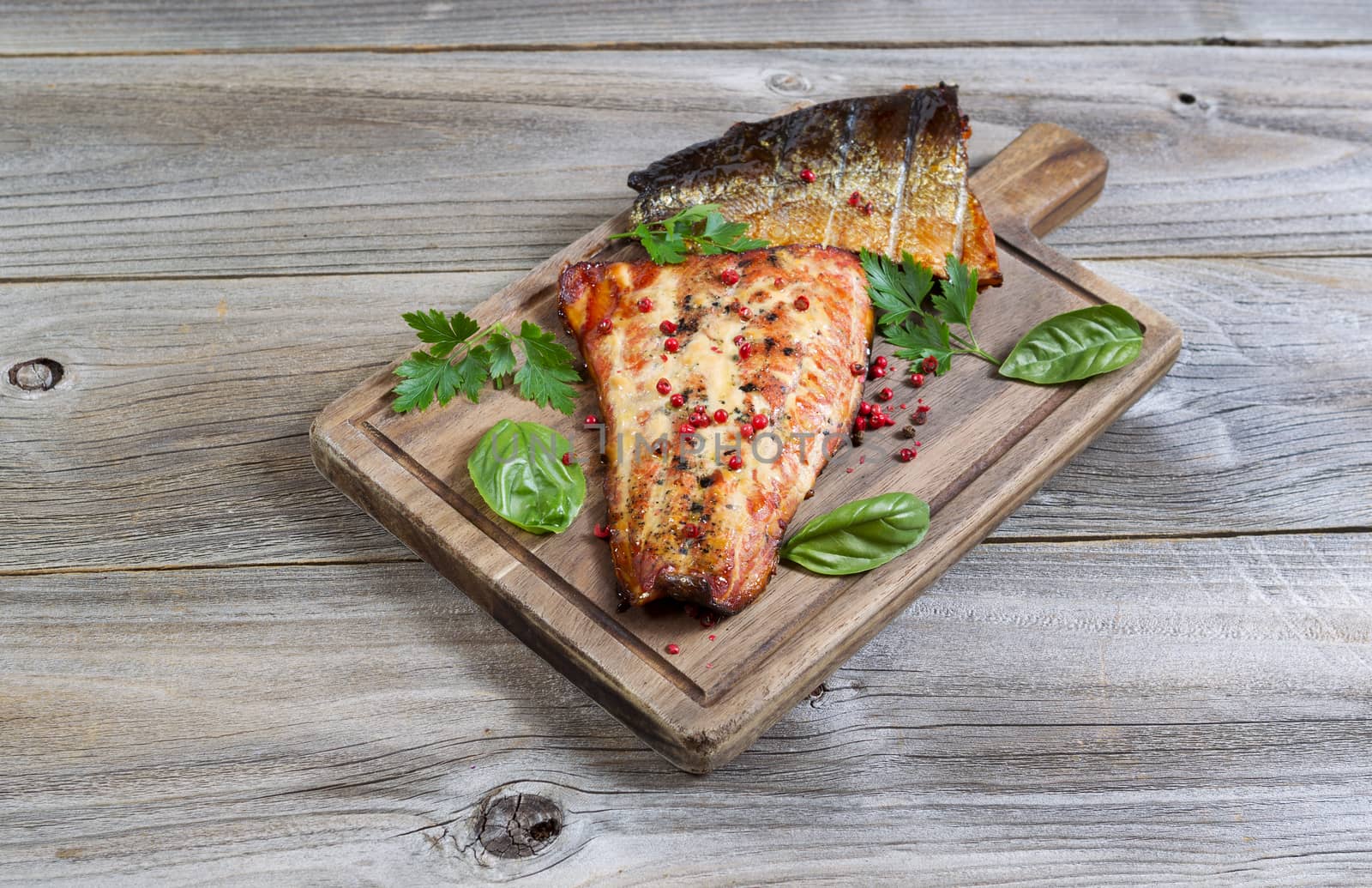 Horizontal view of smoked salmon fillets, fresh out of cooker, with seasoning on serving board with rustic wood underneath