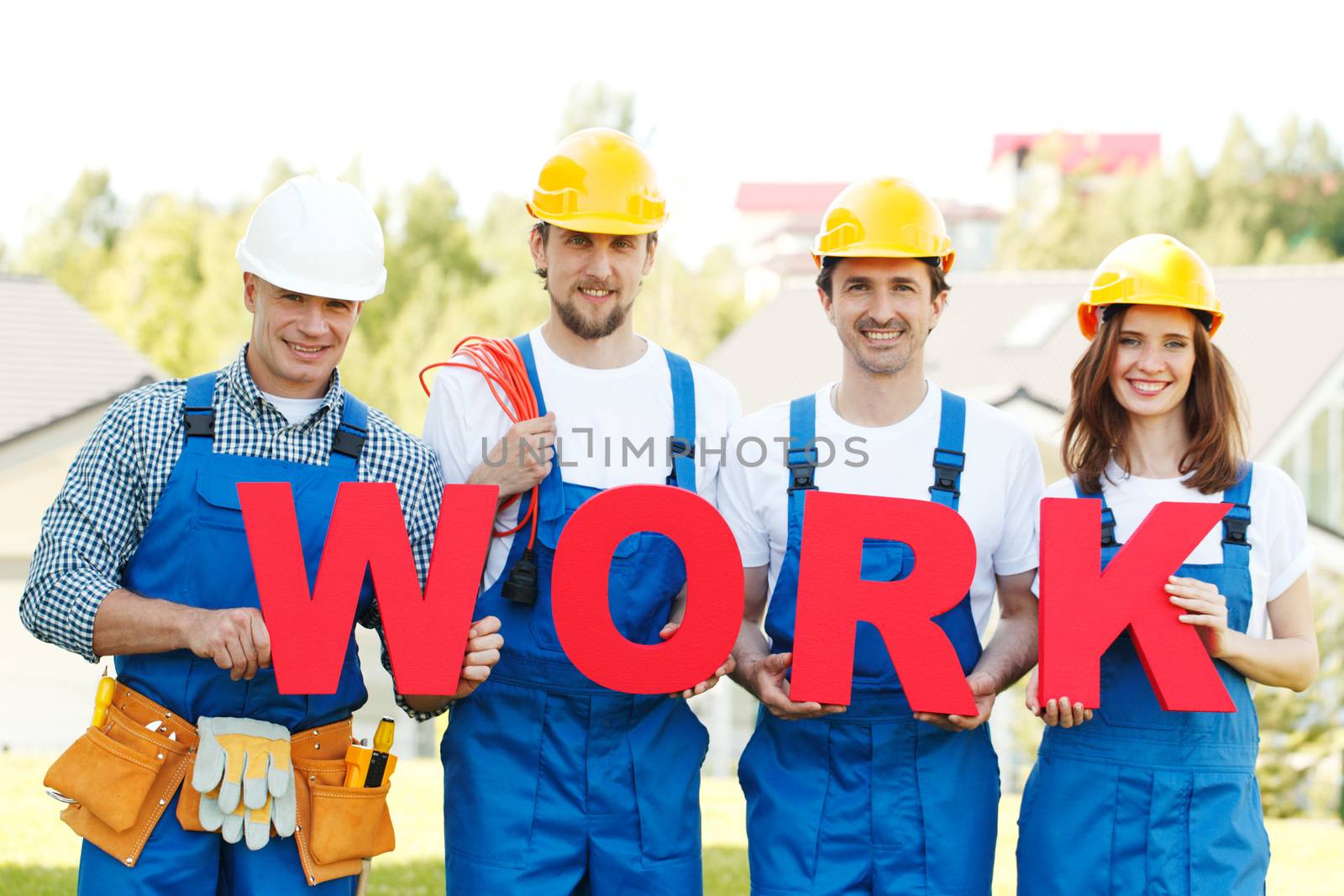 Friendly young team of construction workers with WORK letters outdoors