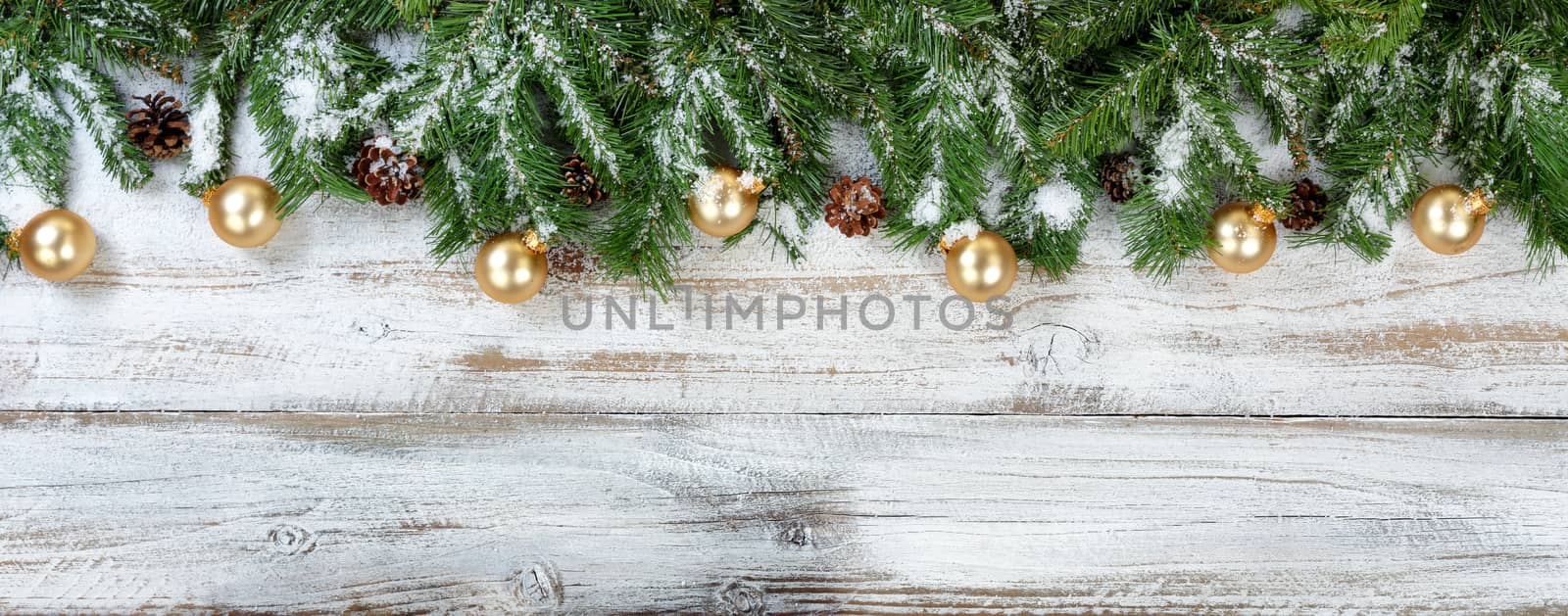 Christmas evergreen branches and golden ornaments on rustic white wood background