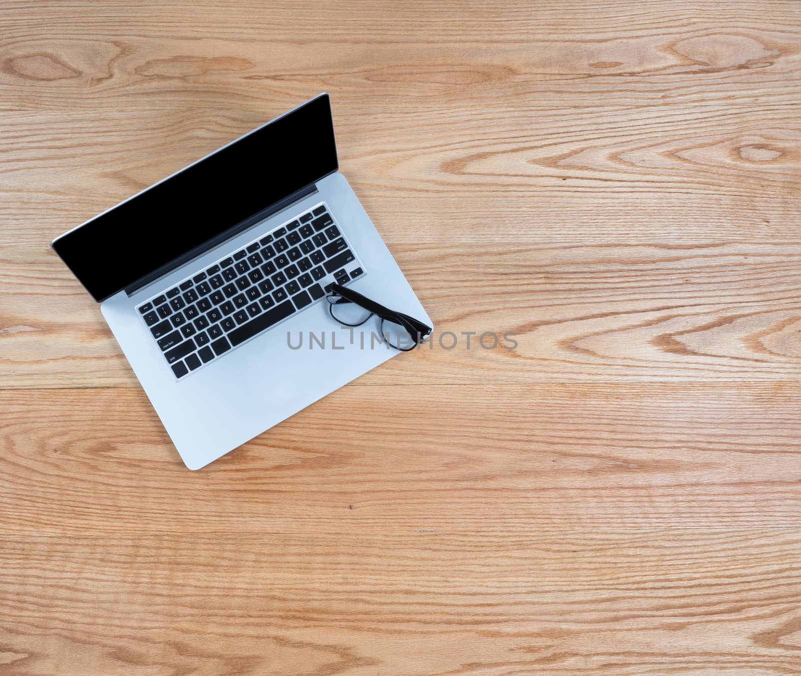 Clean oak wooden desktop with laptop computer and reading glasses 