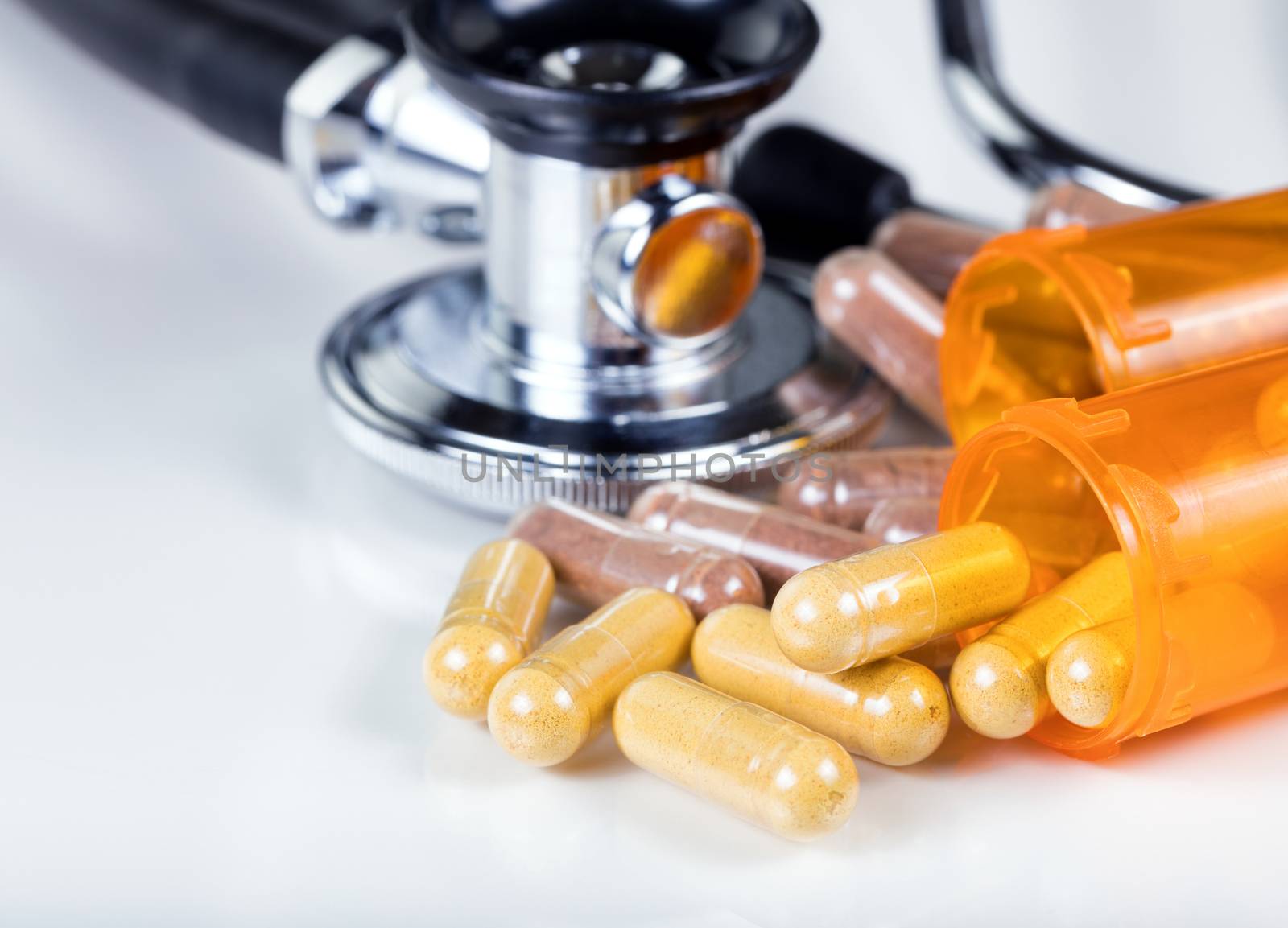 Close up of capsules spilling out of containers with stethoscope in background on white. Selective focus on capsules in front of first bottle. 