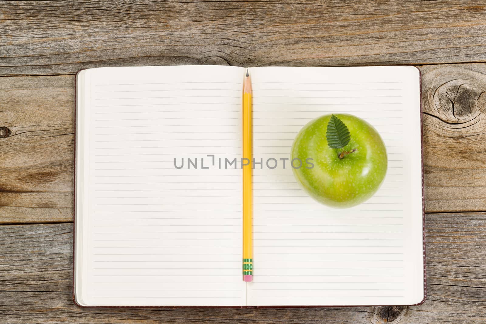 Top view of green apple, open notepad with pencil in center on rustic wood.