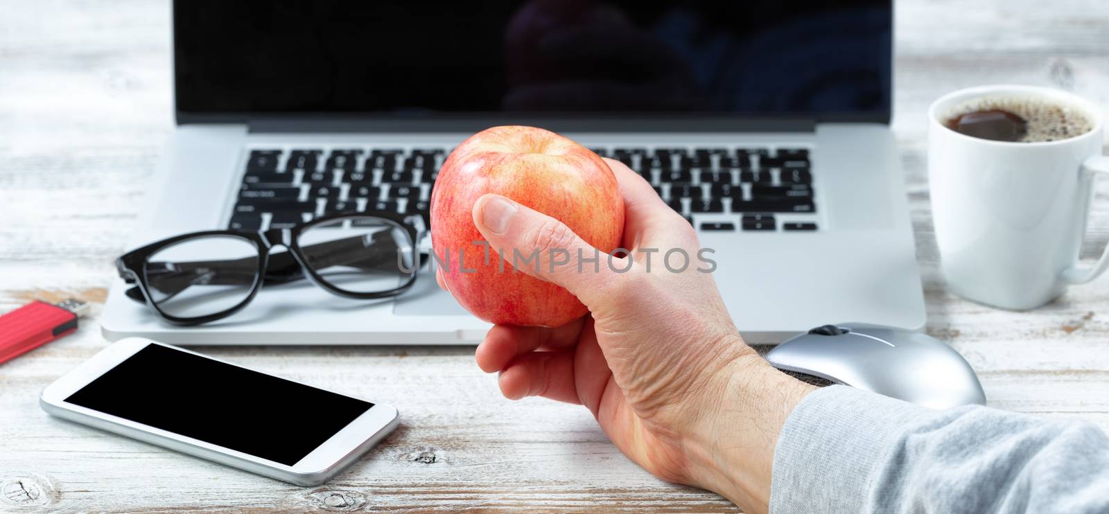 Close of male hand holding fresh apple with workstation technology in background for business or education use 