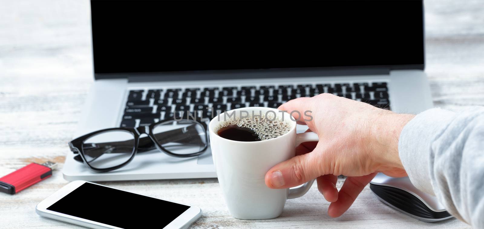 Male hand reaching for a cup of coffee with workstation technolo by tab1962