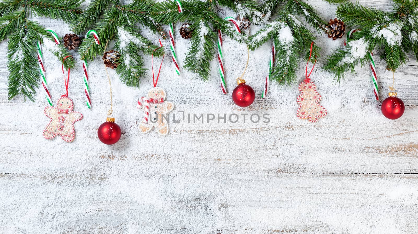 Snowy Christmas evergreen branches with hanging ornaments on rustic white wood background