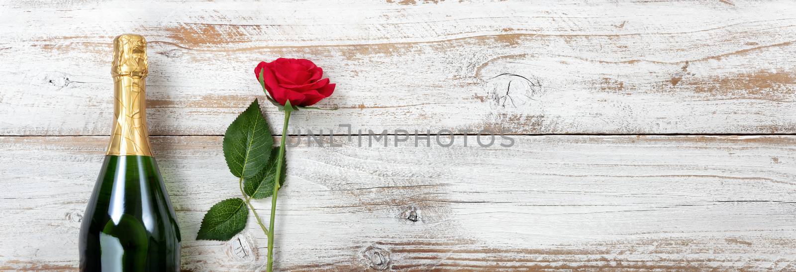 Anniversary background with red rose and champagne on white rustic wood 