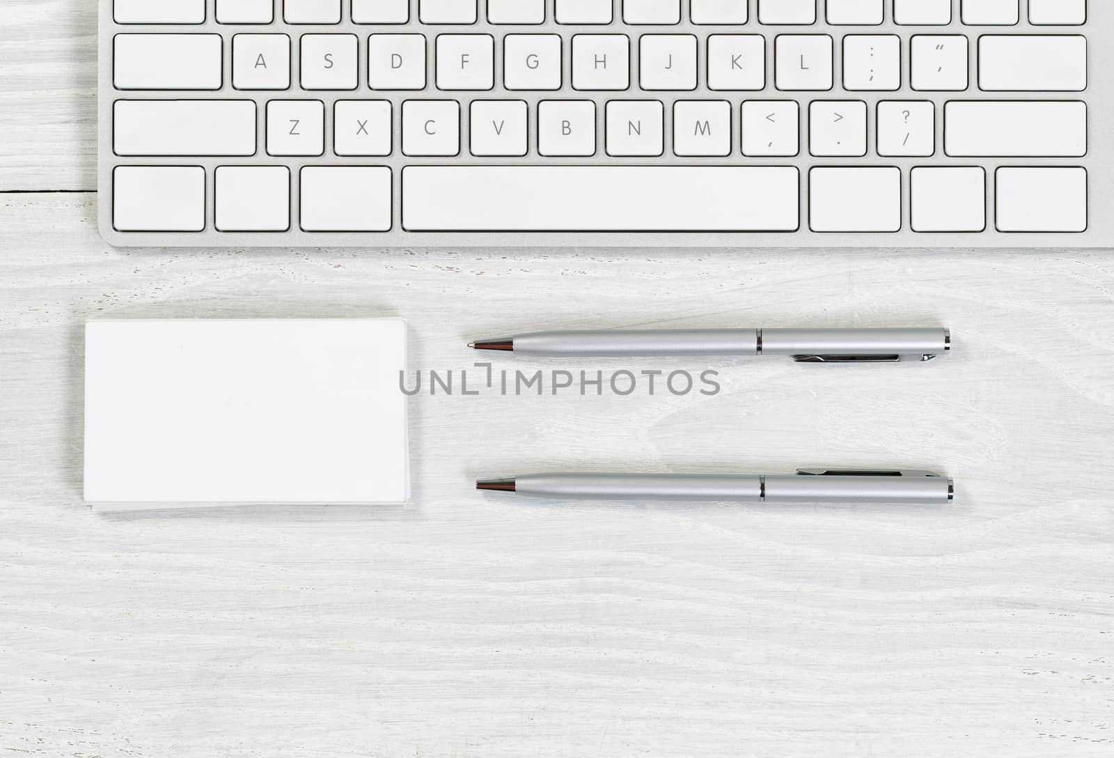 Image of partial keyboard, stack of blank business cards, and silver pens on white desktop. Layout in horizontal format.