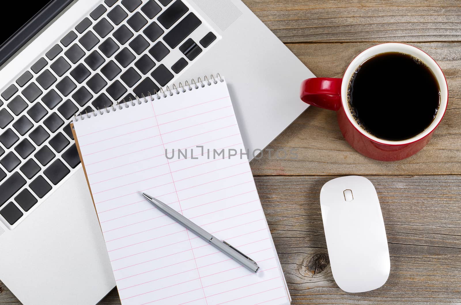 Paper and pen over laptop with coffee and mouse on side of rustic wooden desktop. 