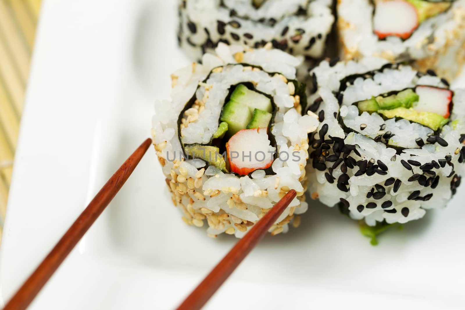 Closeup horizontal photo of a single inside out California roll being picked up with chopsticks   