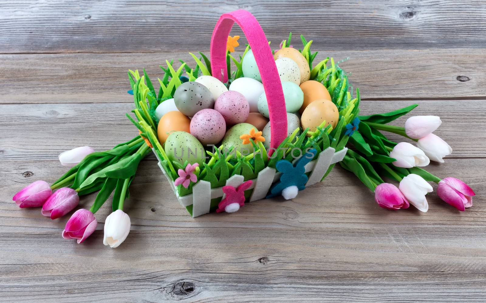 Carry basket filled with colorful eggs and pink tulips on weathered wooden boards for Easter background  