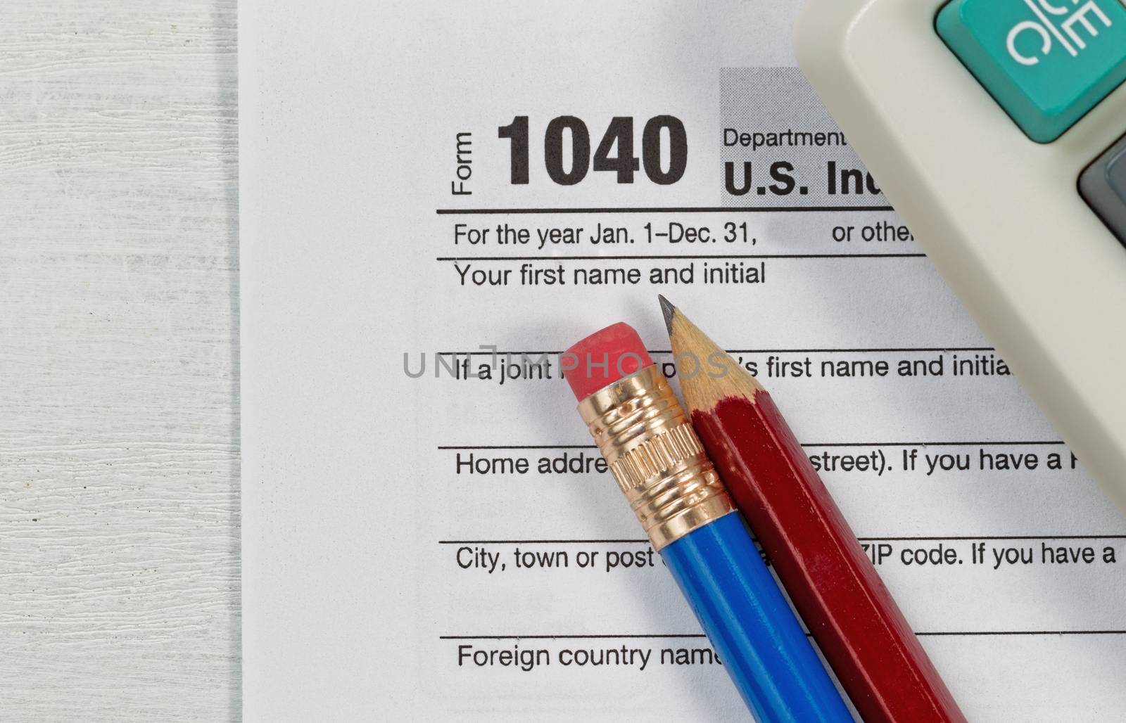 Close up U.S. Individual tax form 1040 with partial old calculator and pencils on wooden desktop. Focus on pencils.  