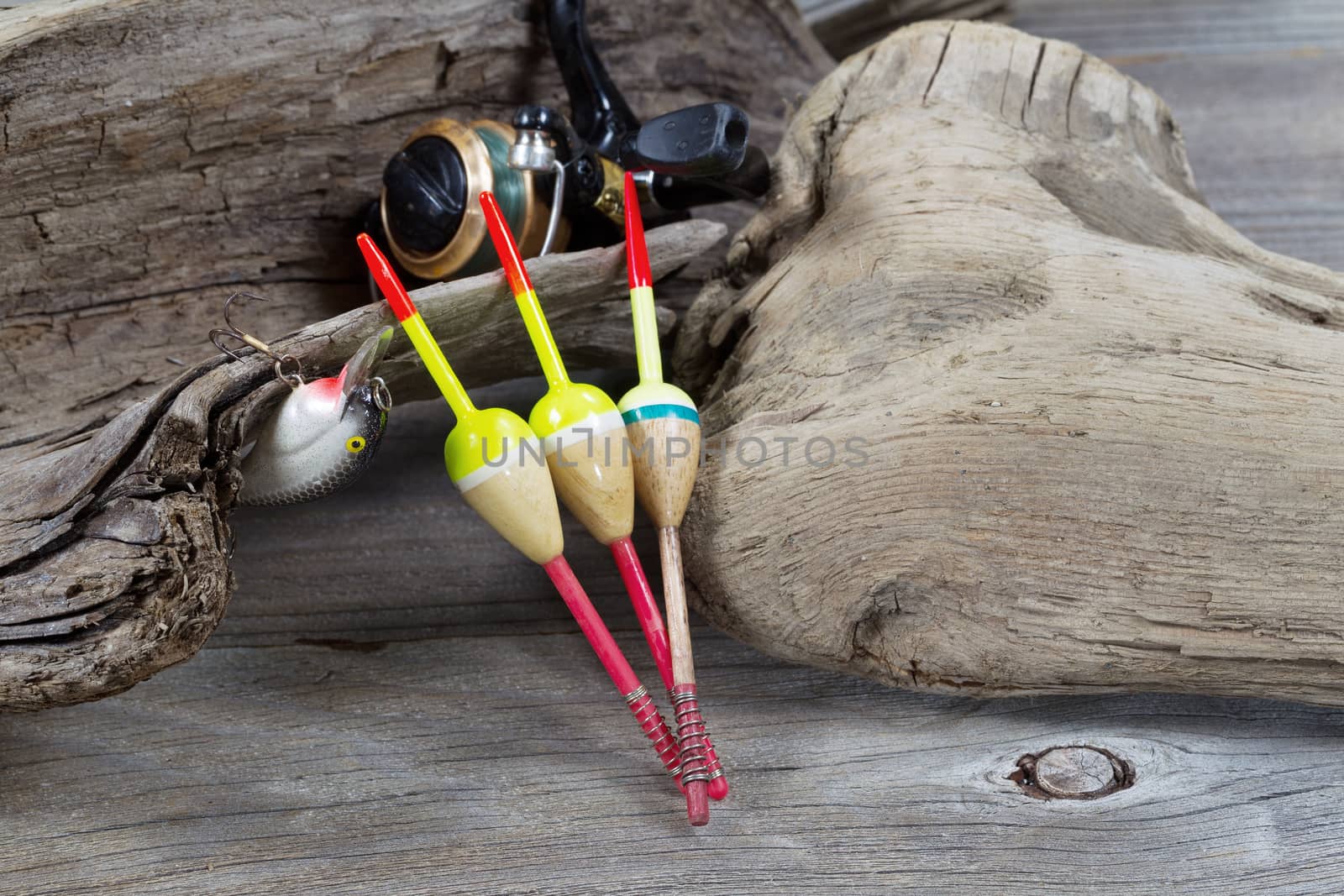 Closeup horizontal image of fishing objects consisting of floats, reel, single lure all resting against aged driftwood 