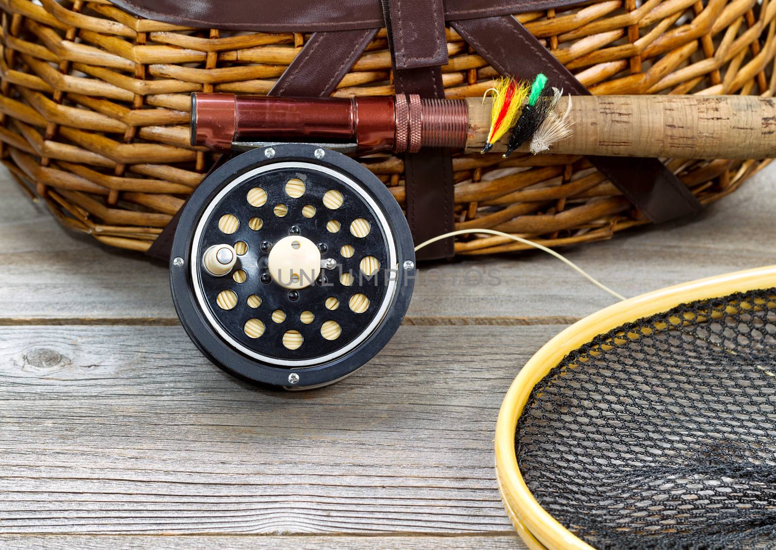 antique fly fishing reel, rod, landing net, creel and artificial flies on rustic wood. Layout in horizontal format.