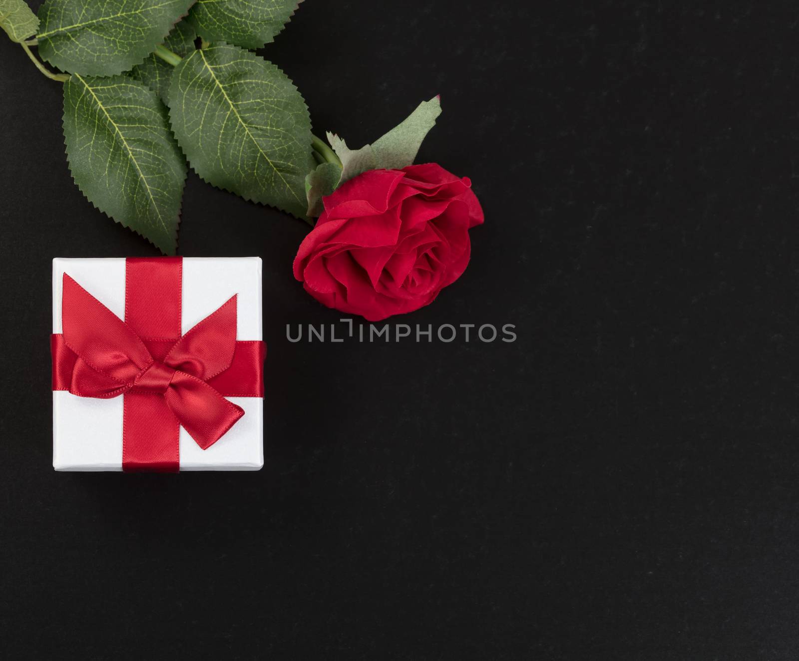 gift box and a single red rose on dark stone background by tab1962