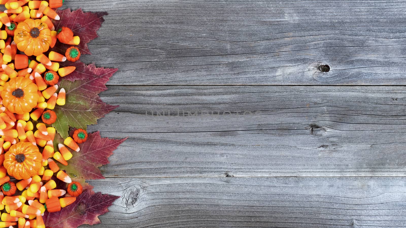 Left border of Halloween candies and Autumn decorations on rustic wooden boards