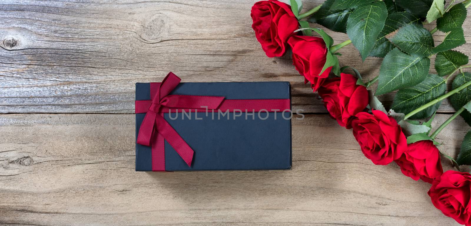red roses and dark gift box on weathered wooden background in flat lay view 