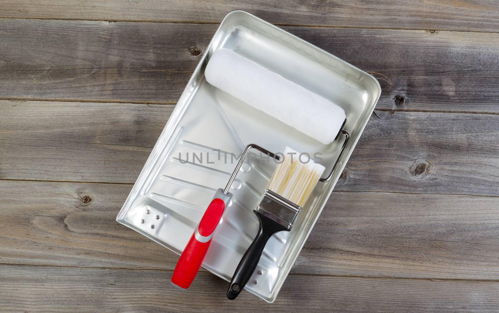 Overhead view of new painting accessories on rustic wood consisting of paint brush, roller cover, pan, and hand roller frame