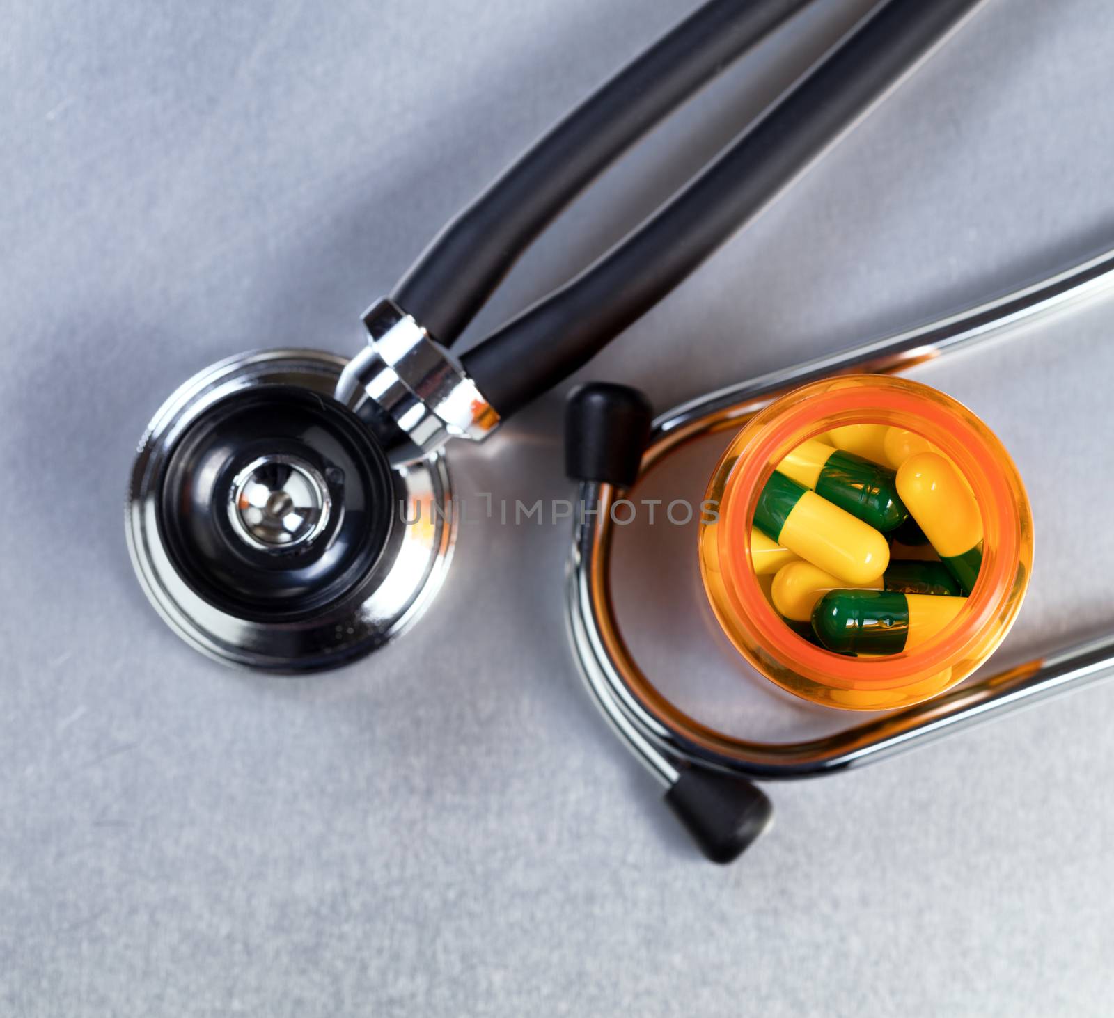 Top view of medicine bottle filled with capsules and stethoscope in background on stainless steel table 