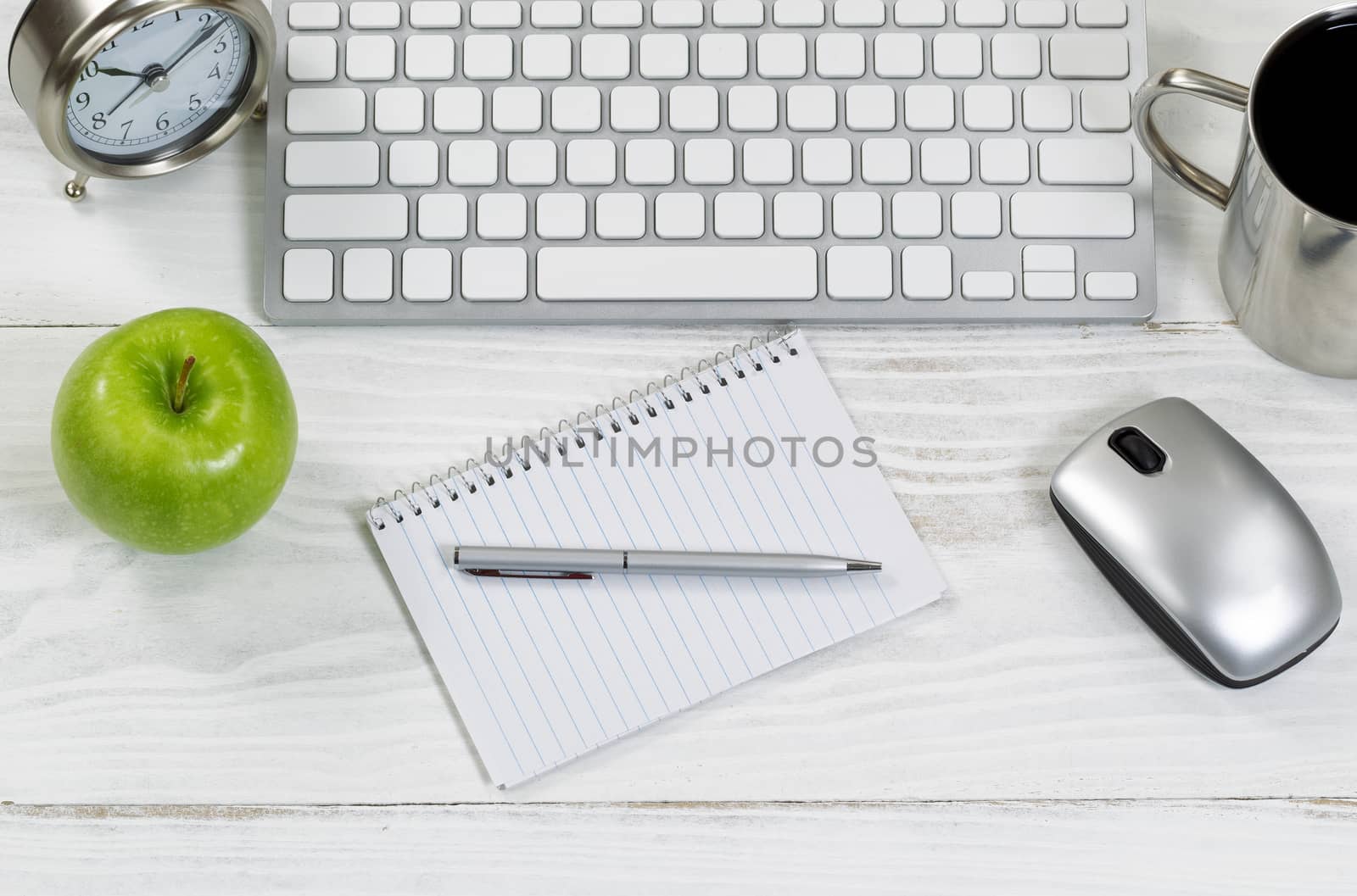 Top view of organized white wooden desktop with office work objects. Layout in horizontal format with mostly silver objects. 