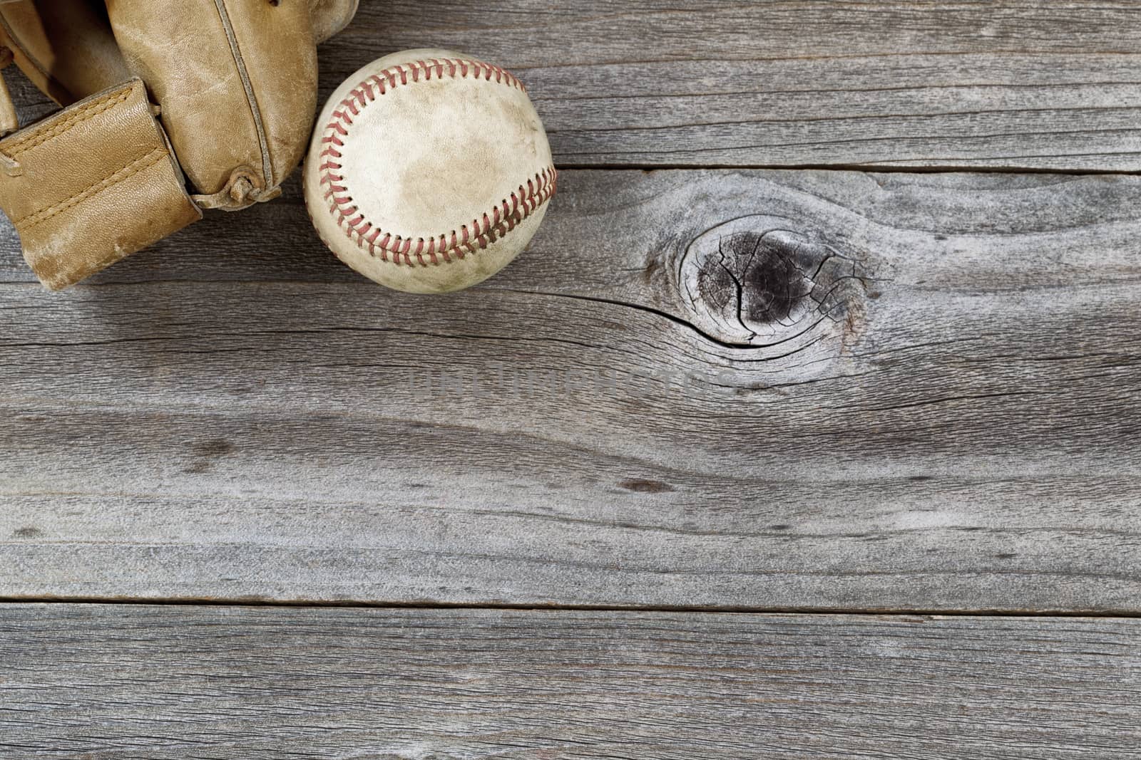 Horizontal top view angle of old baseball and weathered leather mitt on rustic wood 