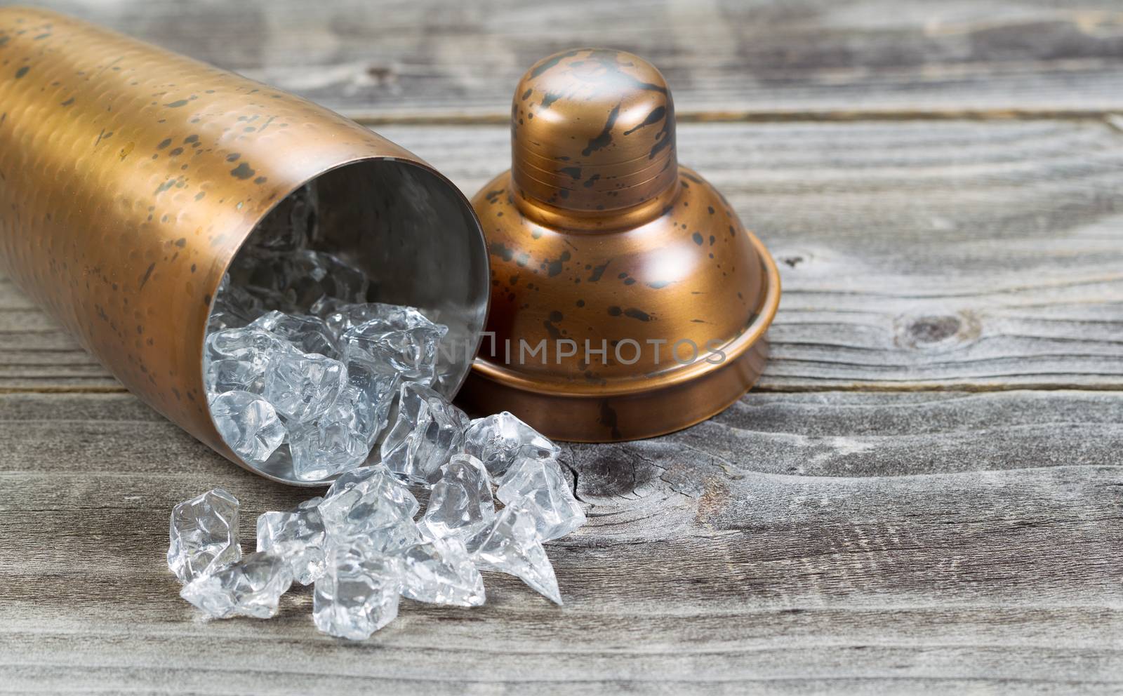 Old metal drink mixer lying on side with crushed ice flowing out onto rustic wood