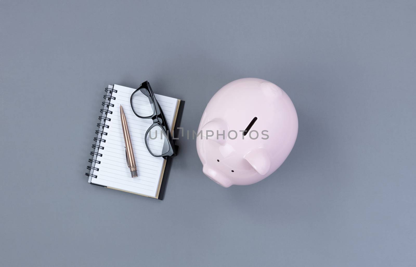 Piggy Bank and traditional writing stationery on gray desktop 