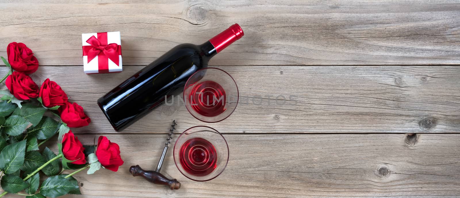 red roses and wine in lower left corner on rustic wood in flat lay view