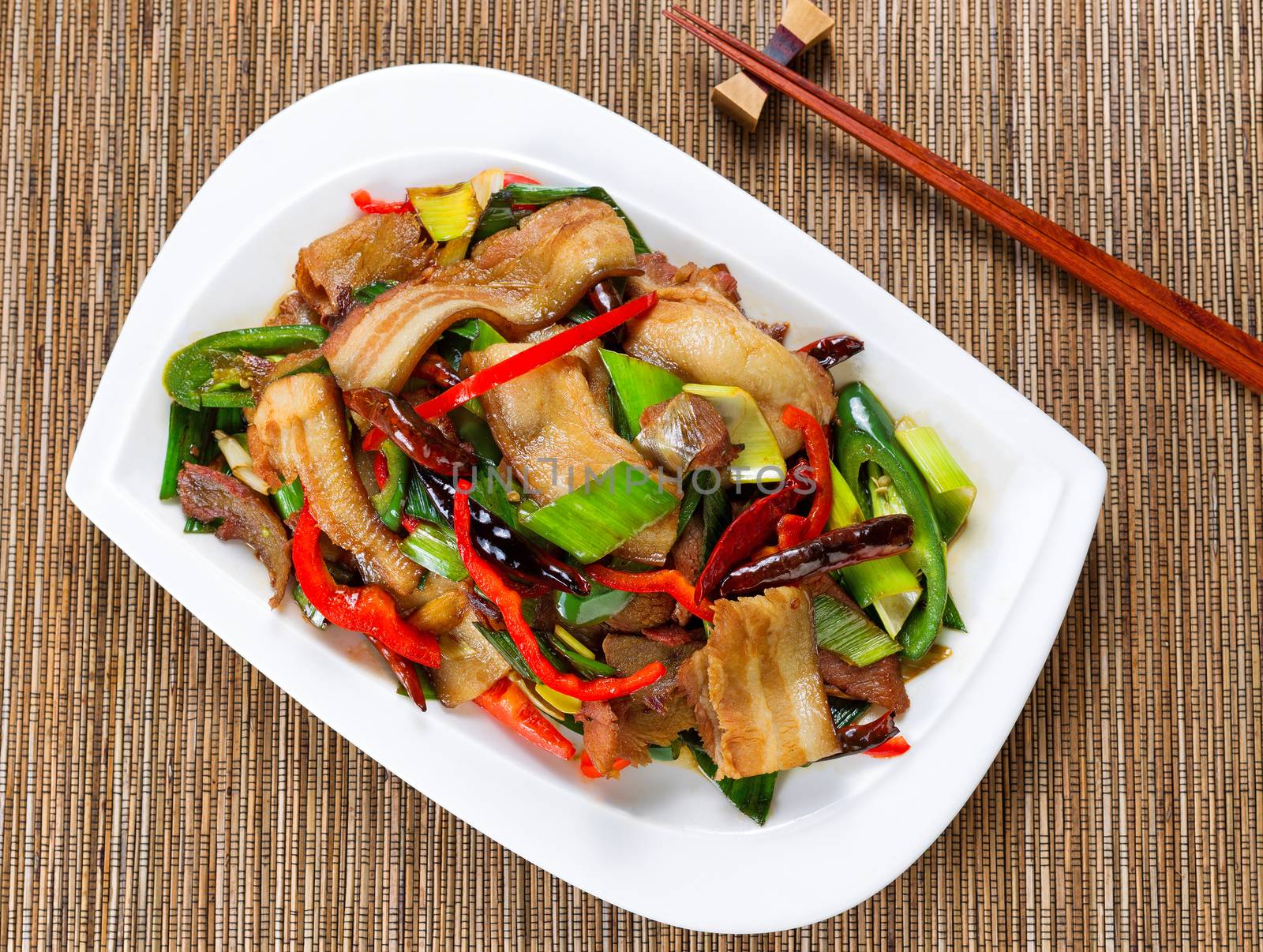 Top view of bacon, beef, peppers and onion in white plate with bamboo mat underneath.  