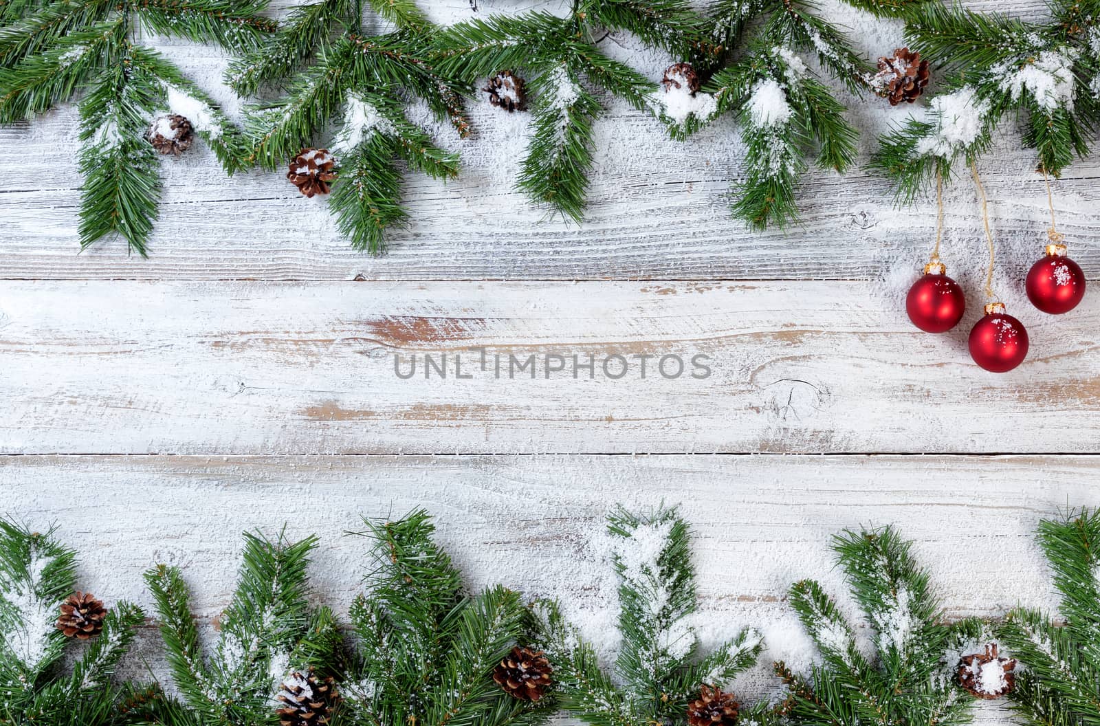 Snowy Christmas branches with red ornaments on rustic white wood by tab1962