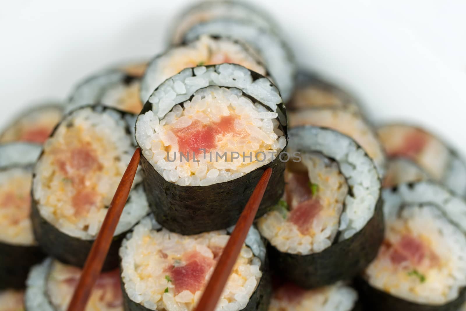 Closeup horizontal photo of a single spicy tuna roll on top of sushi stack being picked up with chopsticks   