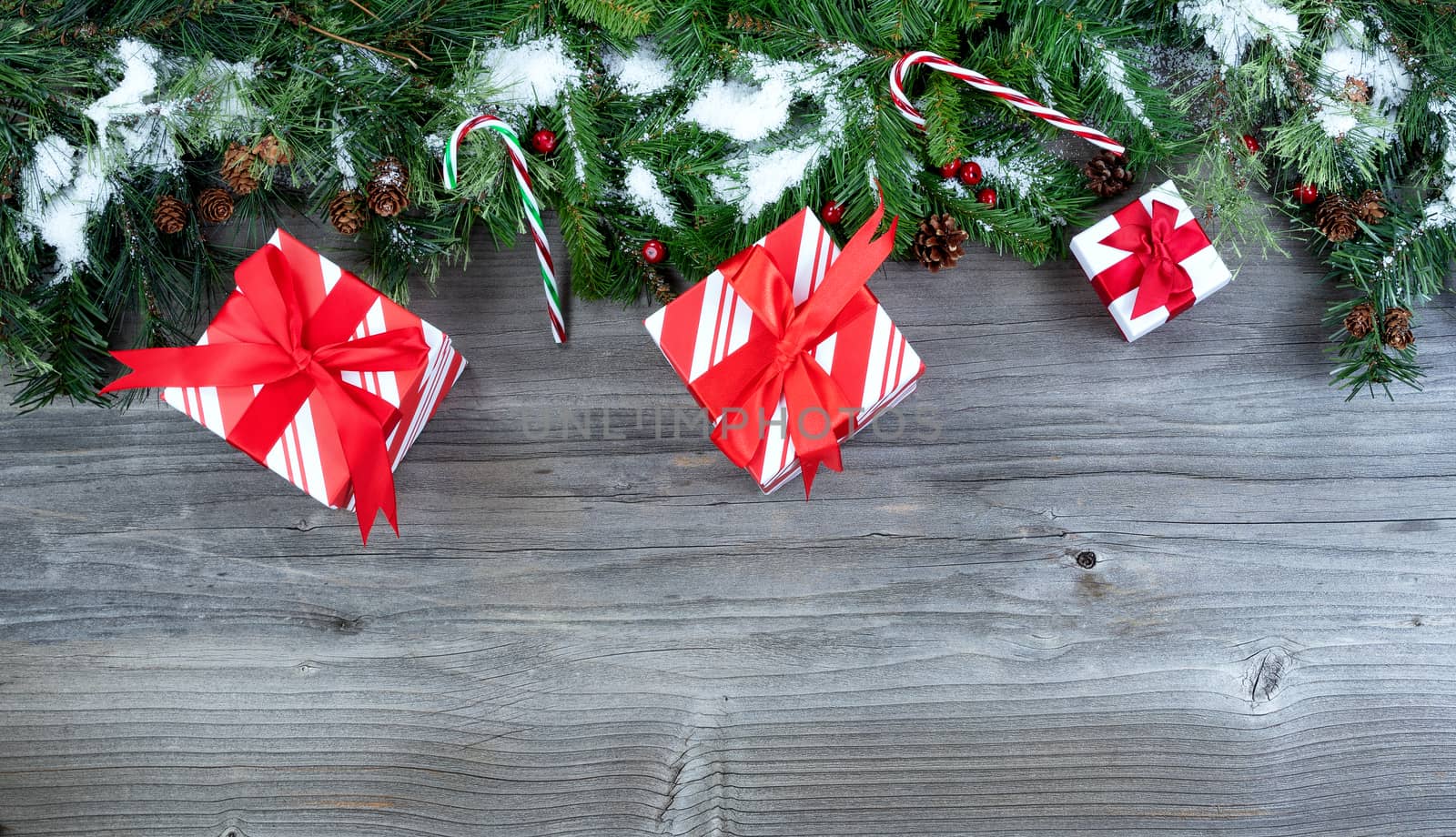 Snow covered Christmas tree evergreen branches with gifts placed on top of a rustic wooden background  