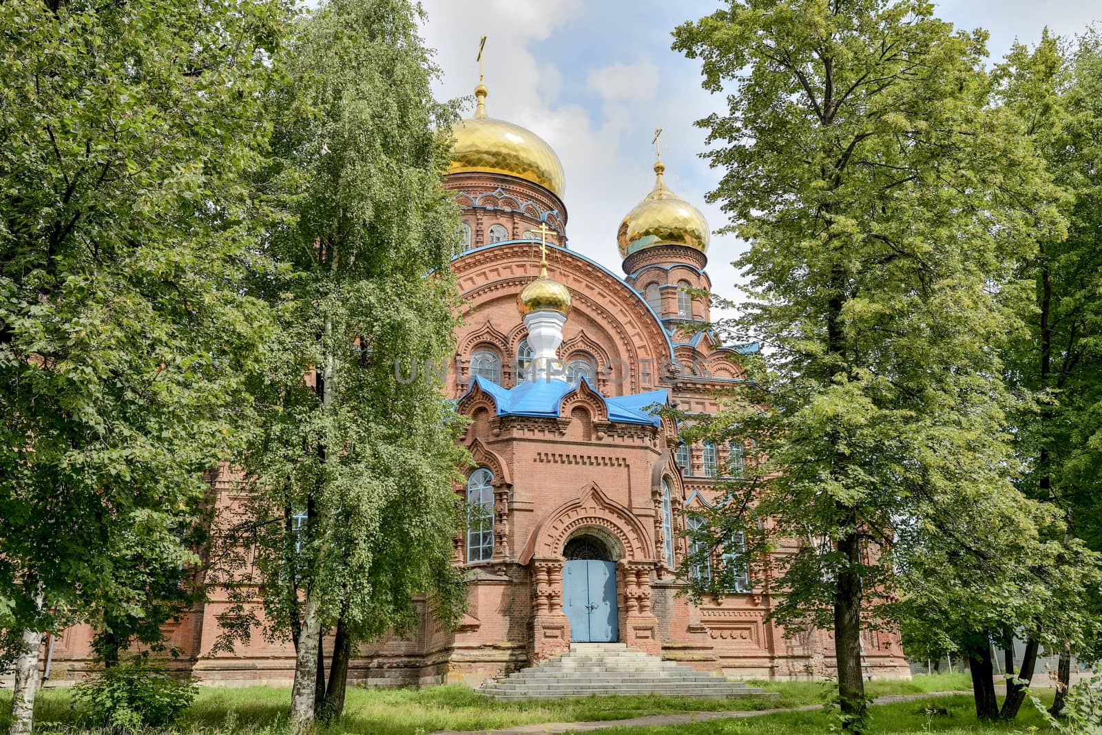 Ancient orthodox church of red brick with golden domes and a blue roof.
