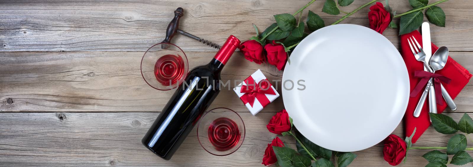 Holiday Dinner setting with red wine and roses on rustic wood in flat lay view