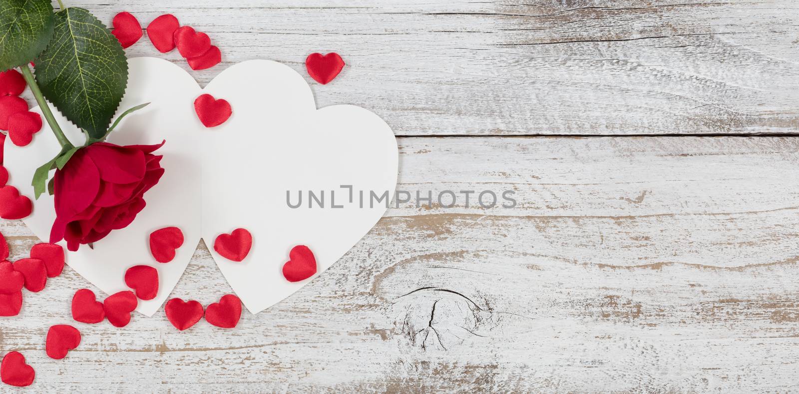 Valentines card with red heart shapes and a single rose on rustic white wood in flat lay view