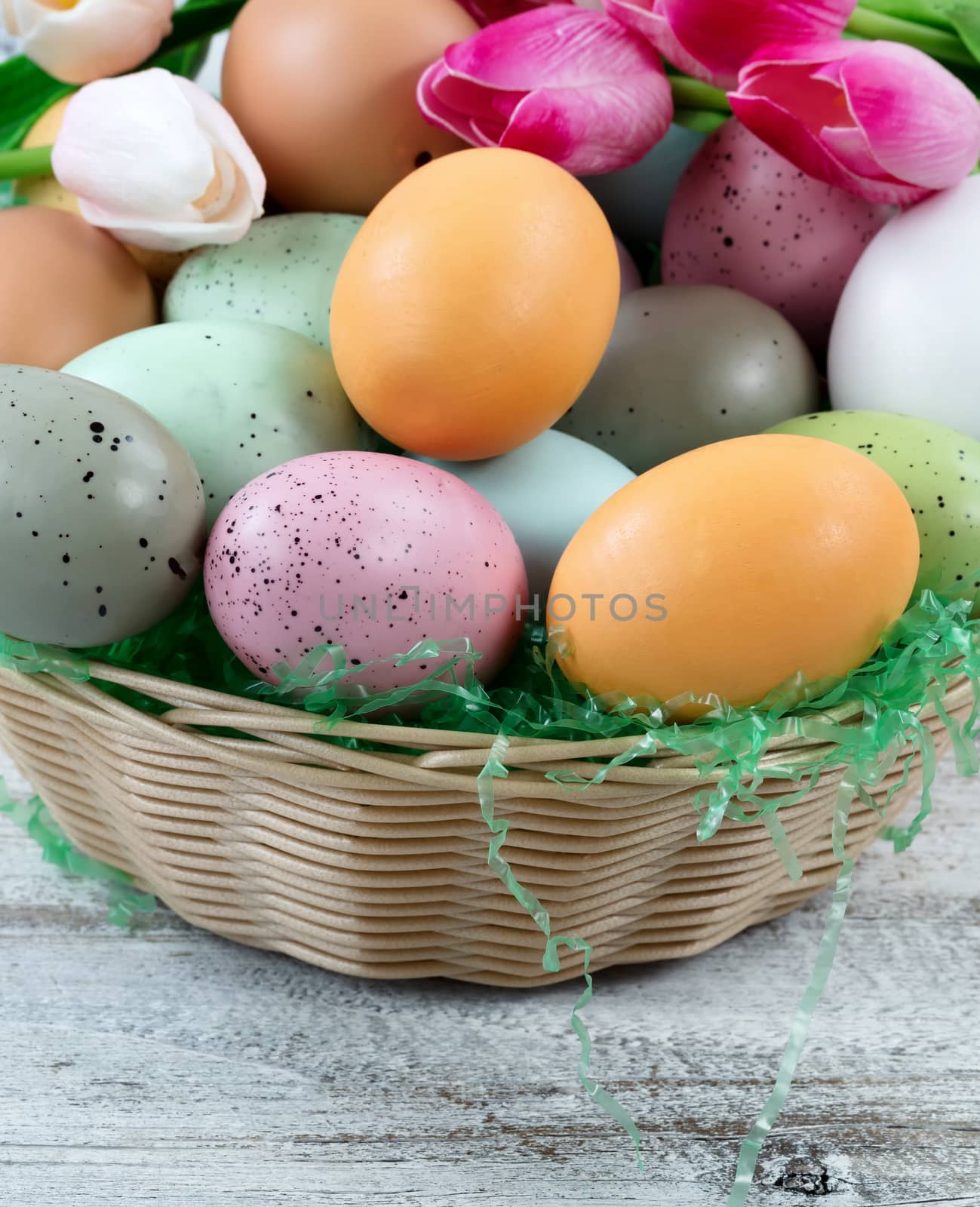 Basket filled with colorful eggs and tulips in background on rustic white wood for Easter concept 