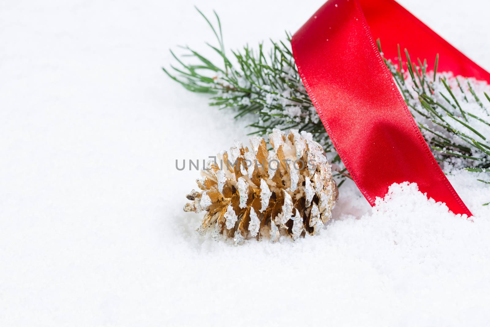 Closeup front view of golden pine cone with red ribbon and fir branch covered in snow 
