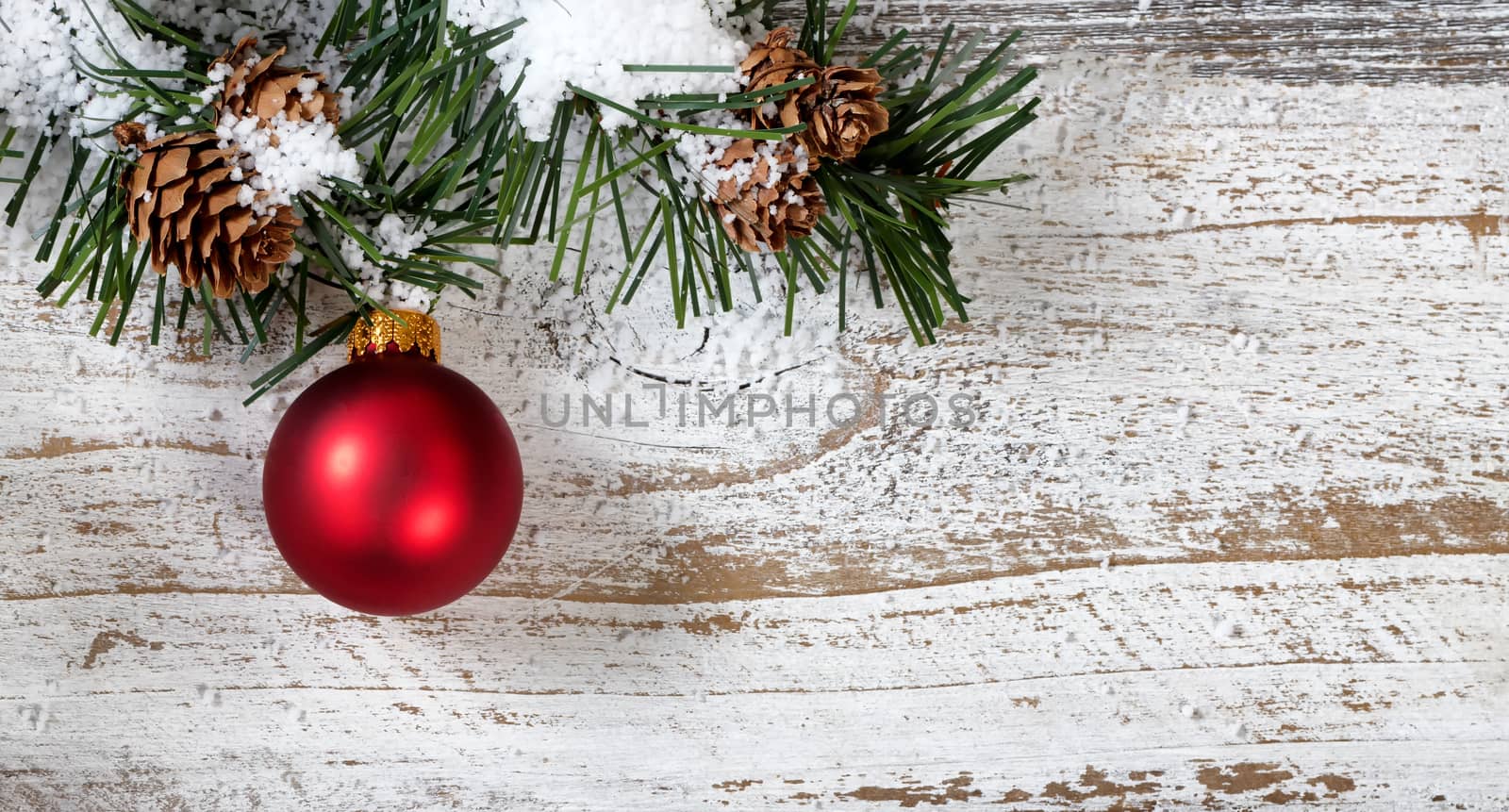 Christmas red ornament hanging in rough fir tree branch on rustic white wooden background