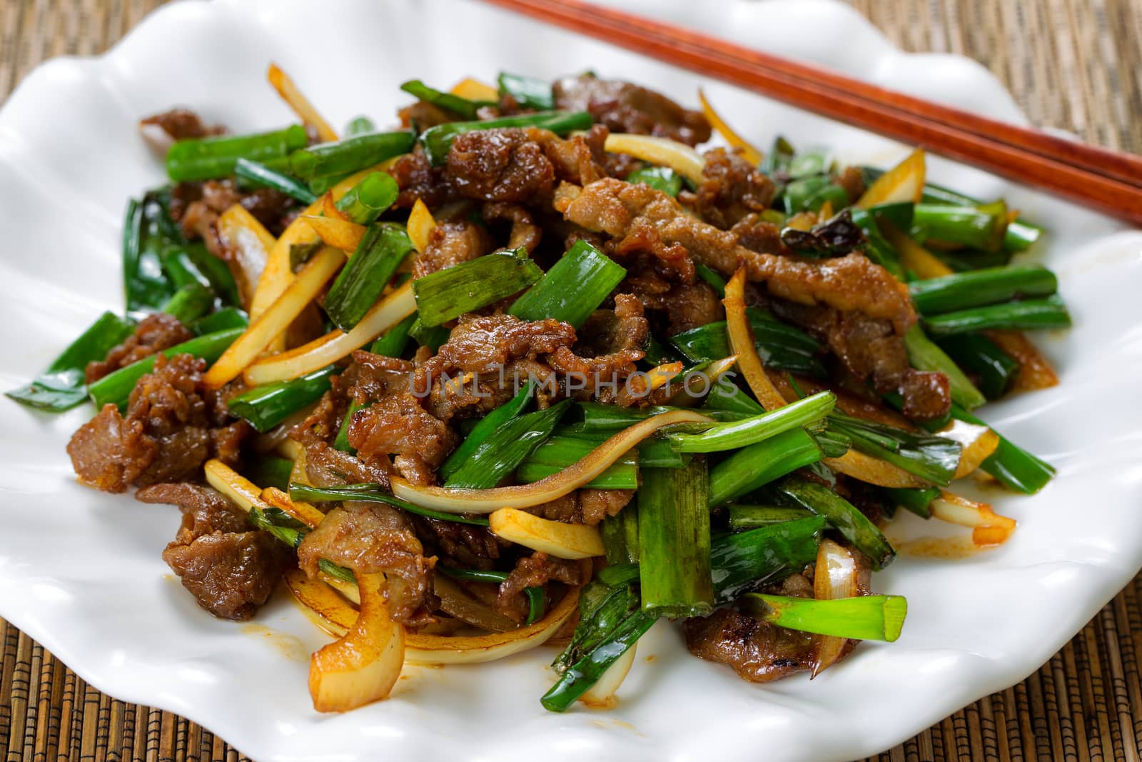 Close up view of beef and green onions in white plate with bamboo mat underneath.  